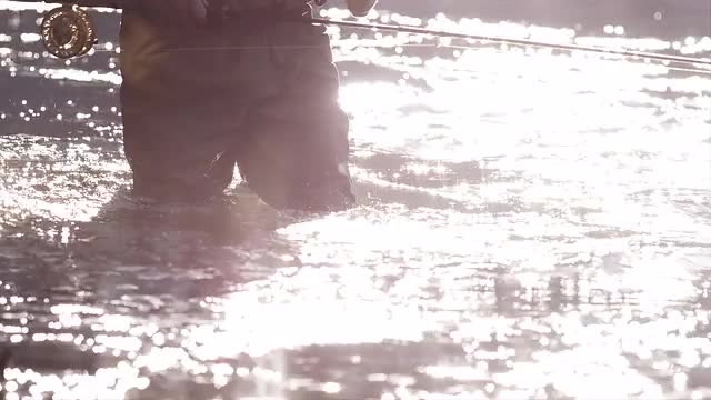 Close up shot of a man walking through rushing water while fly fishing