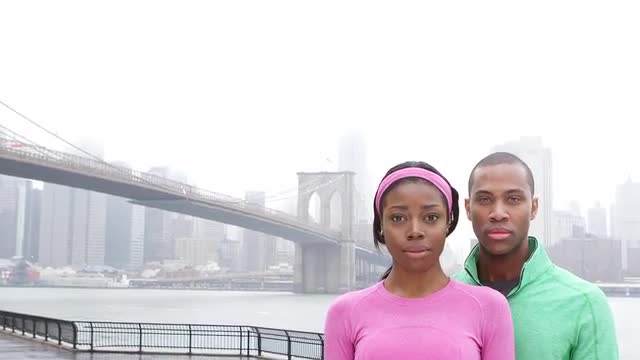 Close up of a man and woman in running gear looking into the camera on an overcast day while standin