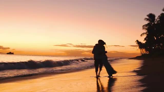A silhouetted couple hold each other and kiss on the beach during magic hour