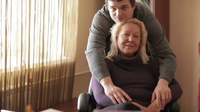Thirty-year-old son hugs his mother looking to the camera.