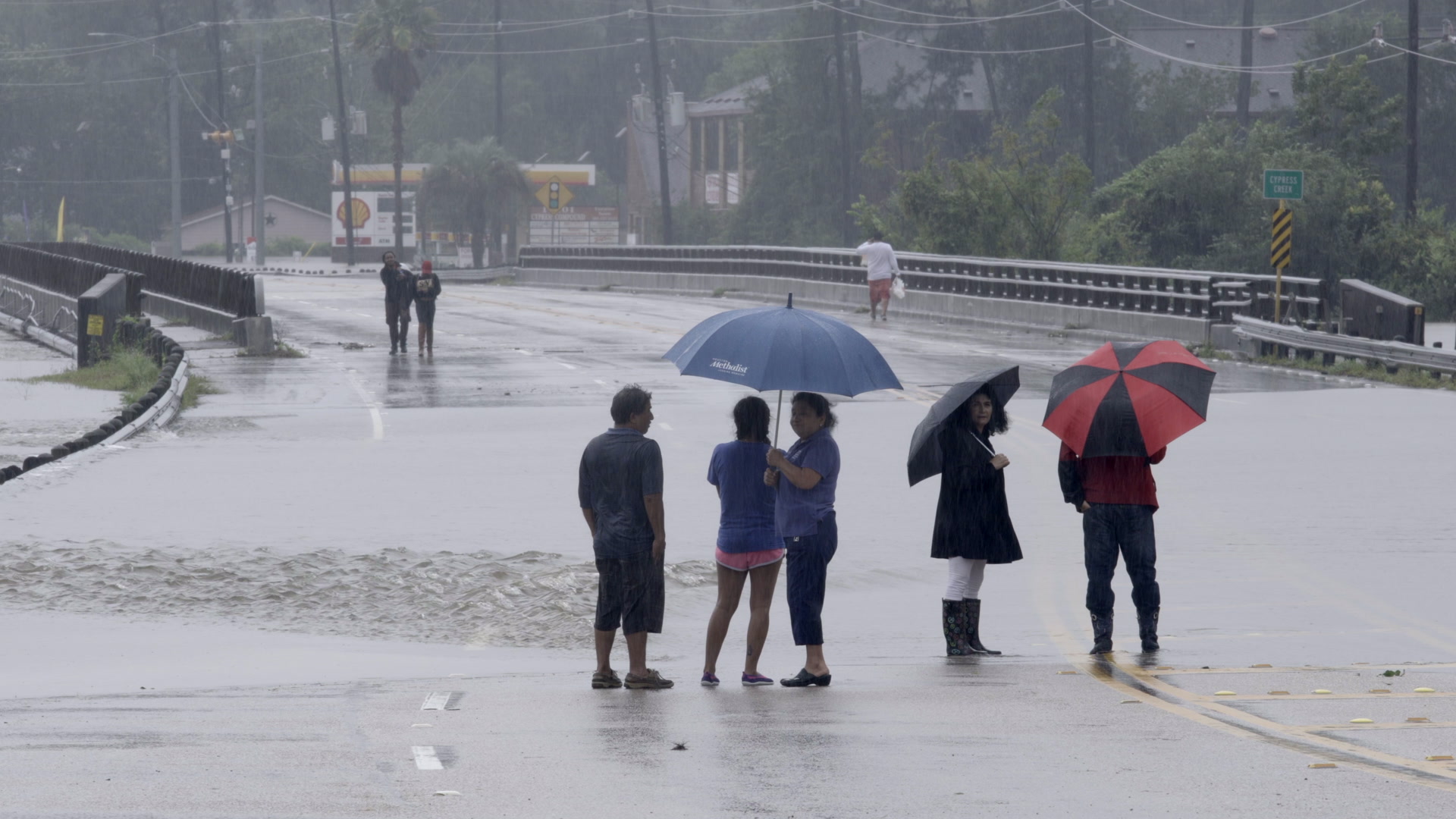 Hurricane Harvey - People with umbrellas watch flooded creek and bridge, 4K