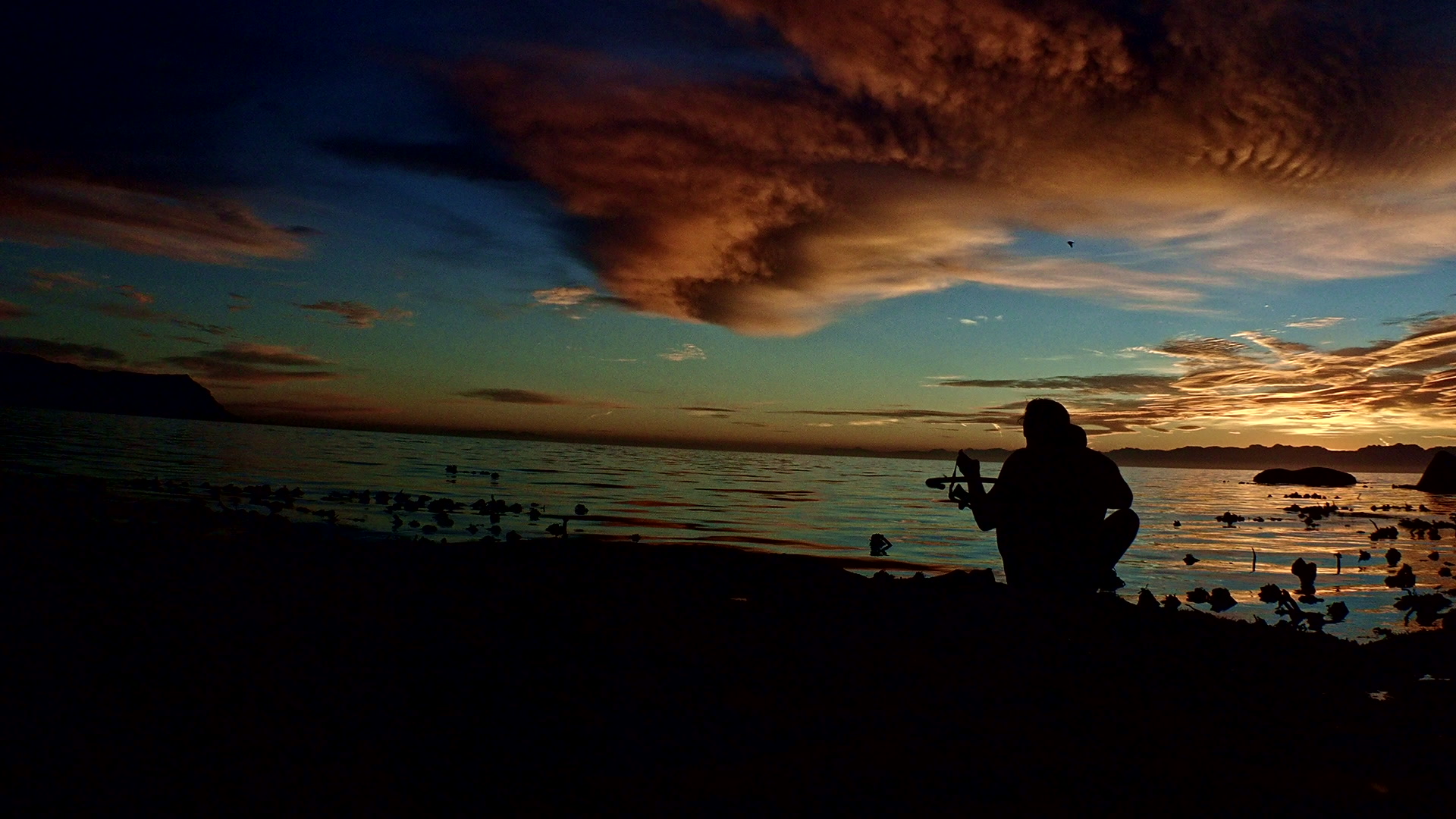 Silhouette of a man carrying snorkelling equipment to the shore at dusk