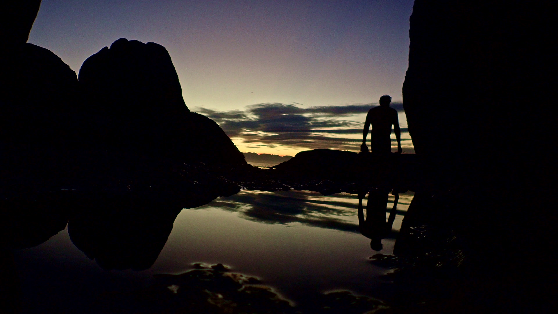 Silhouette of a man carrying snorkelling equipment to the shore at dusk