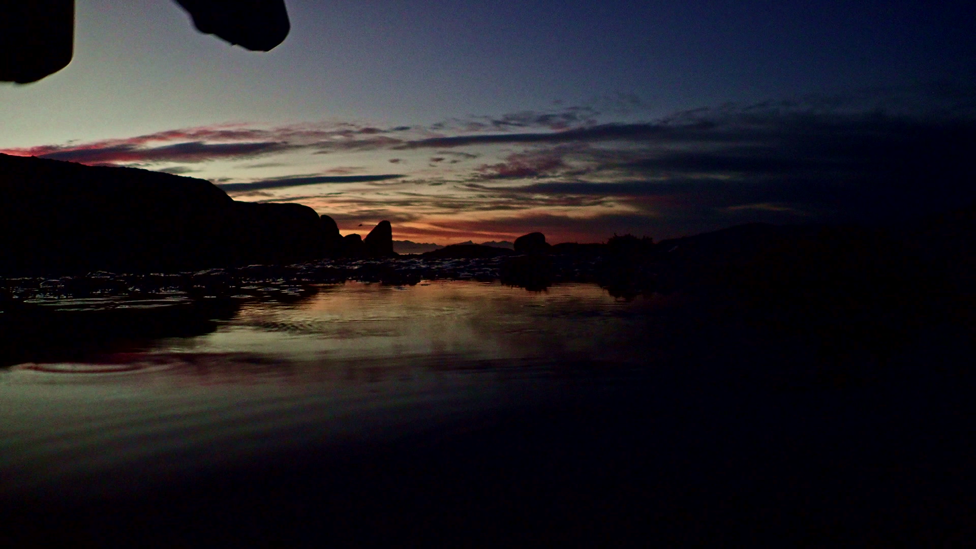 Silhouette of a man carrying snorkelling equipment to the shore at dusk