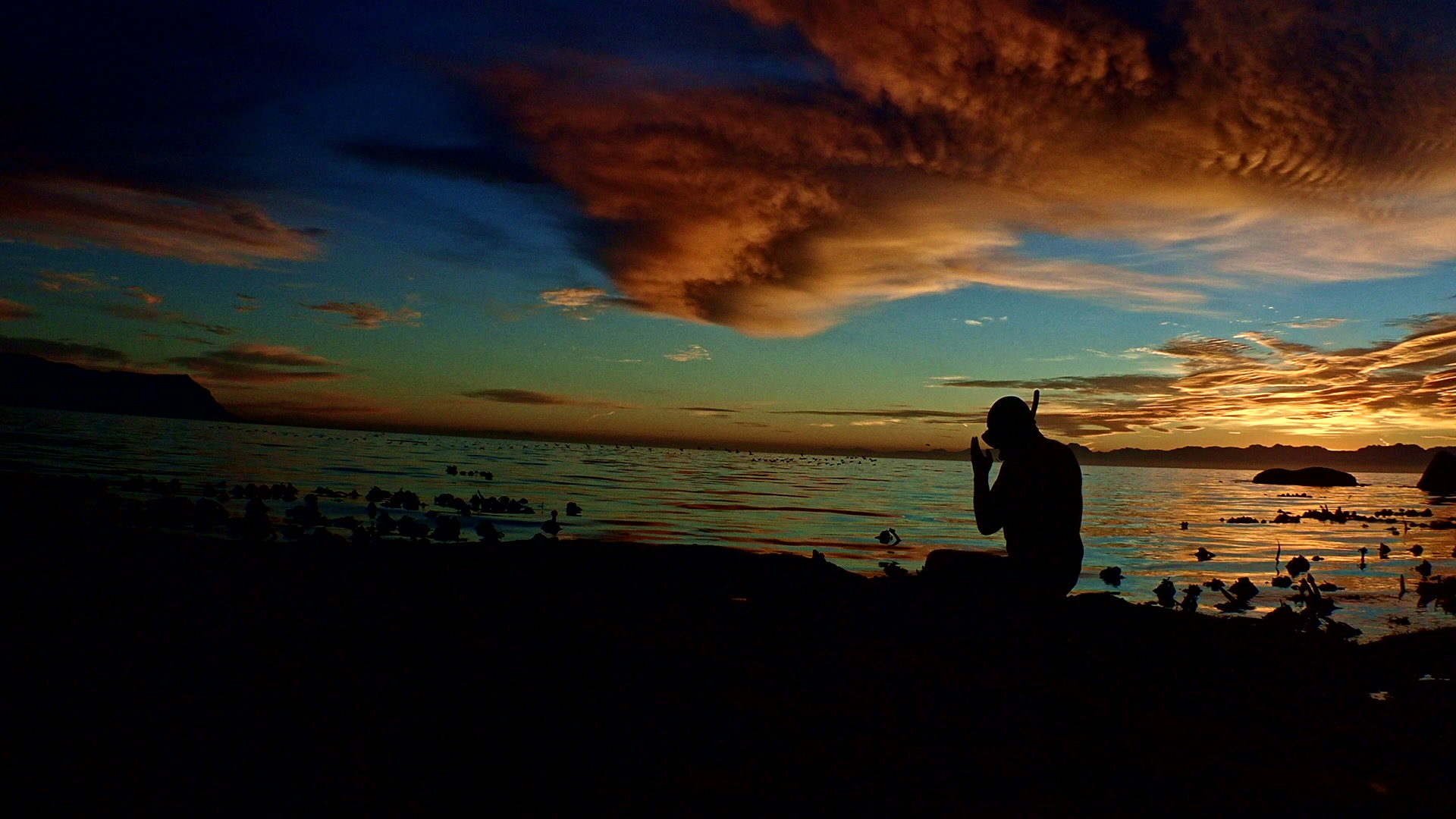 Silhouette of a man putting on snorkelling equipment to the shore at dusk
