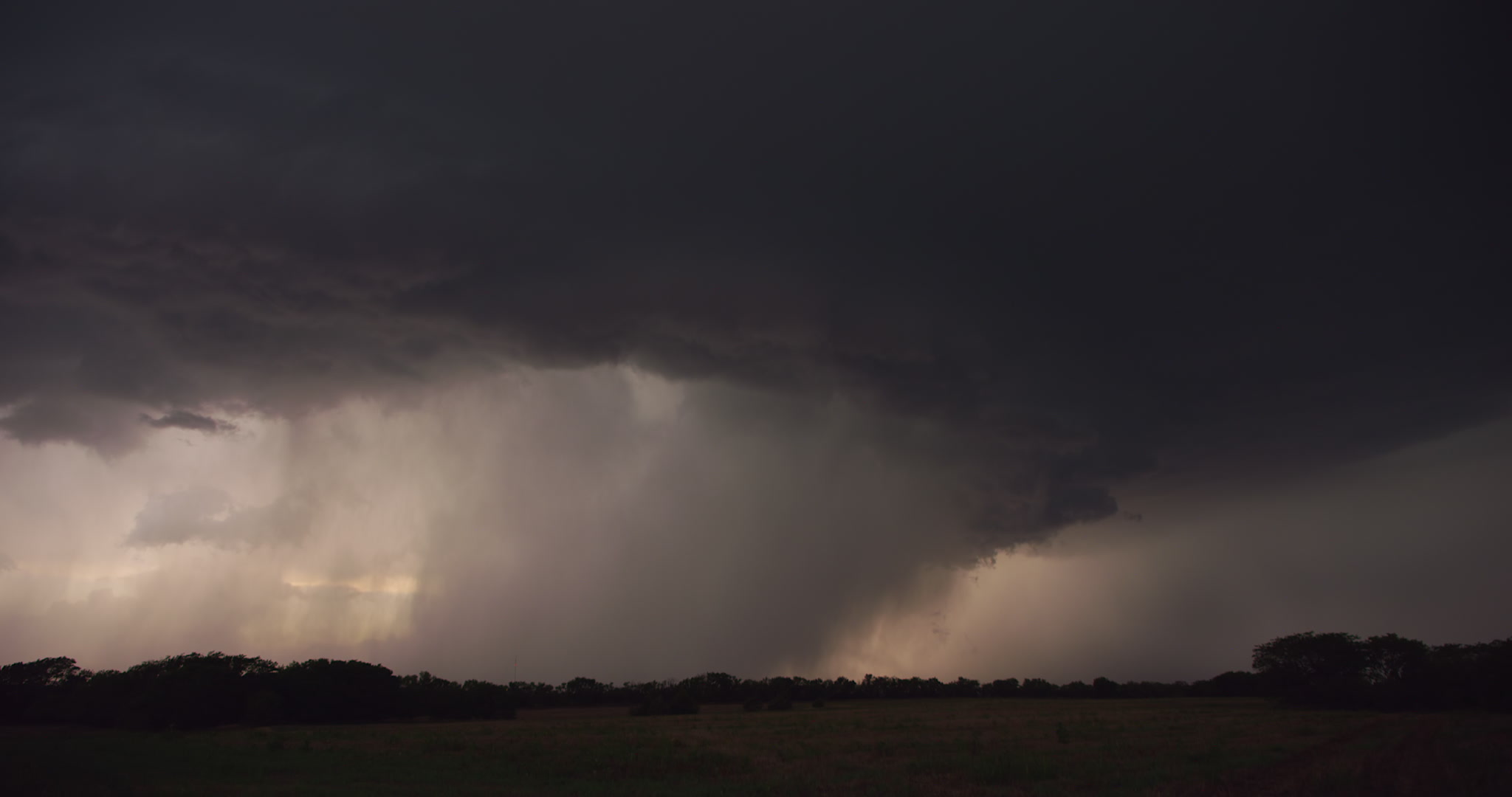 Big, dark thunderstorm approaching over trees and open field, late day, 4K