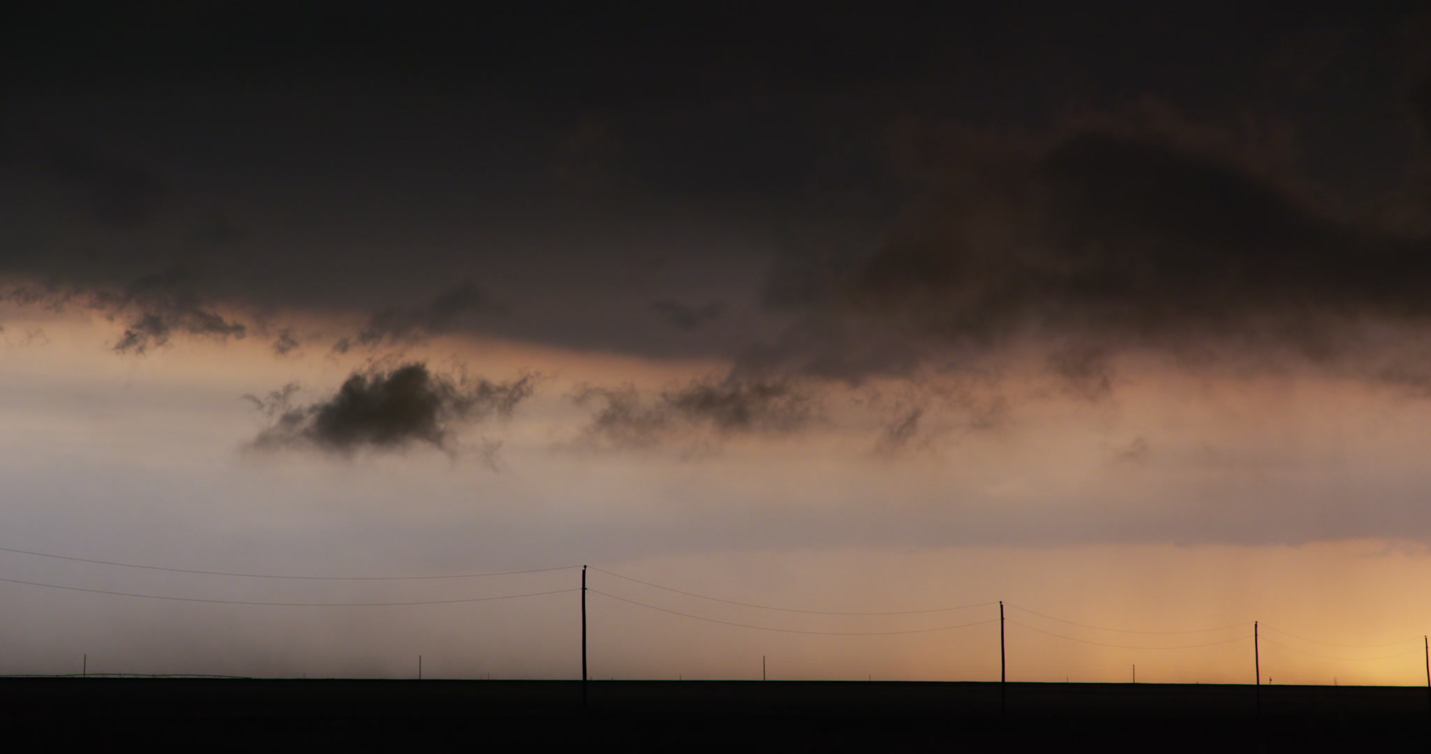 Low, dark storm clouds drift in over rural farm country at sunset, Texas, 4K