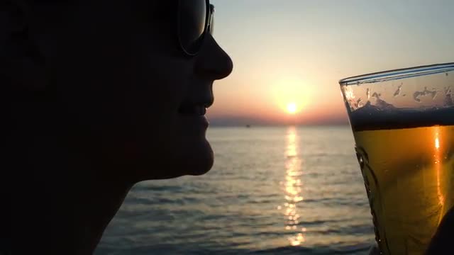 Woman drinking beer on beach at sunset