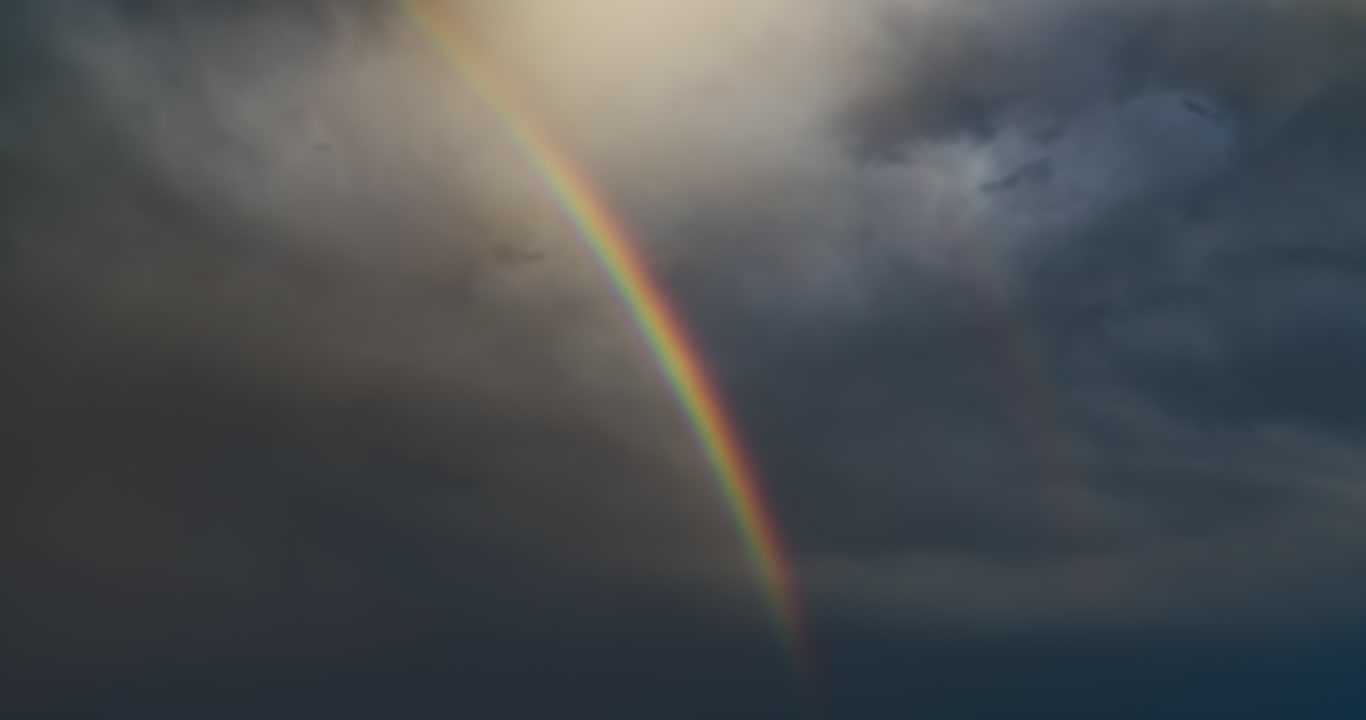 Rainbow segment against dark, stormy sky, close-up, time-lapse, 4K
