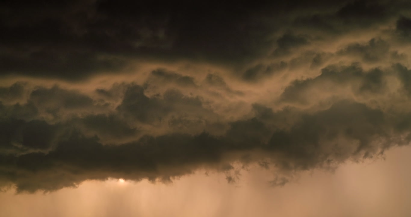 Sun appears briefly from beneath dark, rolling storm clouds, golden hour, 4K