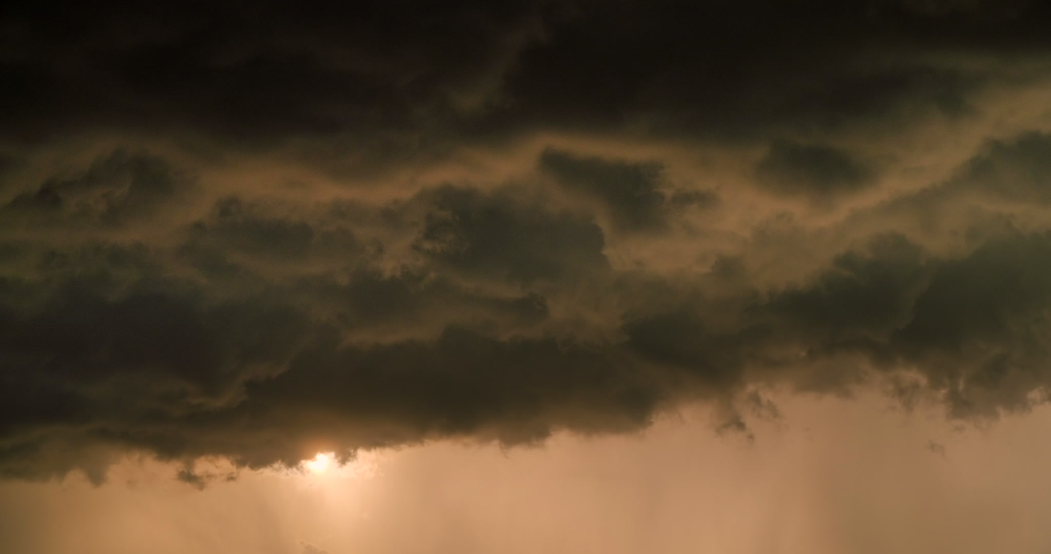 Sun appears briefly from beneath dark, rolling storm clouds, golden hour, 4K