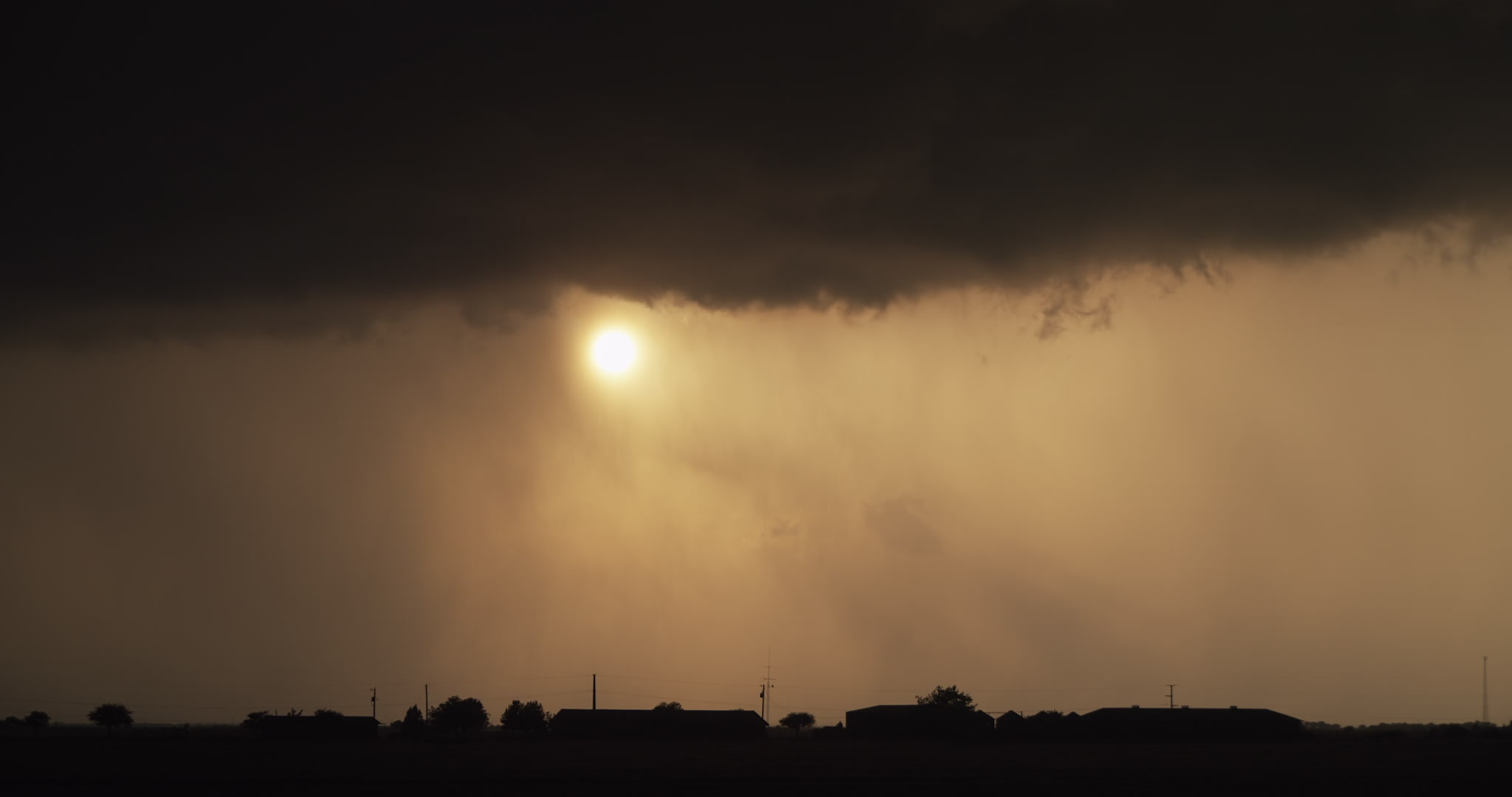 Storm clears, golden sun shines through rain over silhouetted farm below, 4K