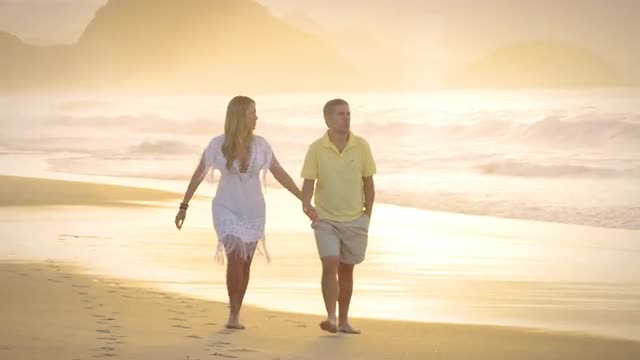 Brazilian couple walk down a beach in Brazil holding hands