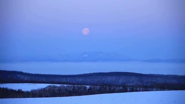 Full moon setting, snow field, and field of clouds in the morning