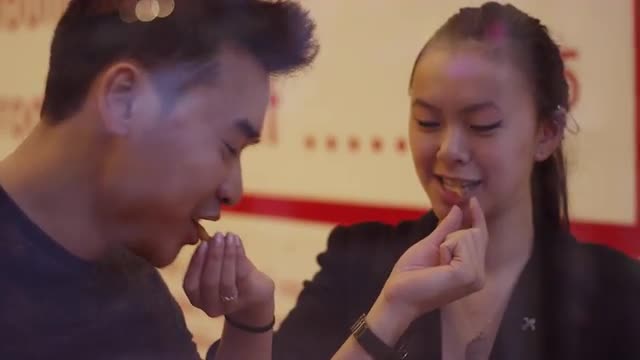 A young couple laughing and eating burgers and fries, through the window