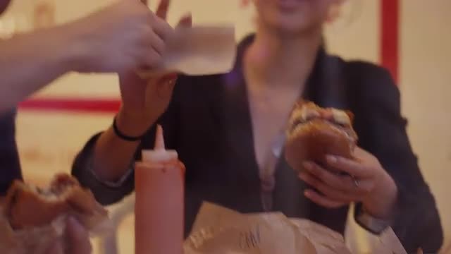 A young couple eating burgers and fries at a restaurant, through the window
