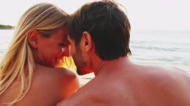 Couple lie on a beach and look out over the ocean at sunset