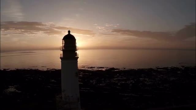 Aerial shot of a lighthouse during a beautiful sunrise in Scotland with coastline in background