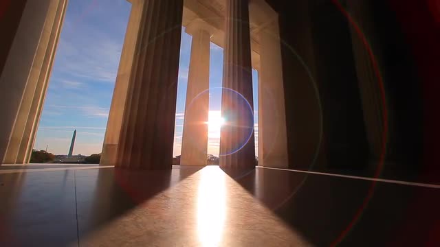A tracking shot with a lens flare of the bottom of the pillars of the Lincoln Memorial.