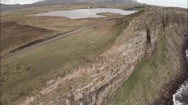Cinematic aerial shot looking over the edge of a cliff on Skye in Scotland with a dramatic coastline