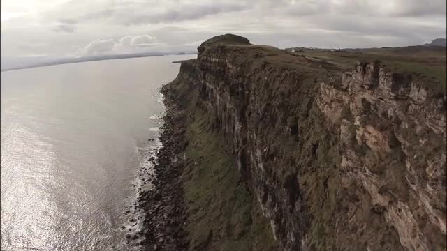 Cinematic aerial shot looking over the edge of a cliff on Skye in Scotland with a dramatic coastline