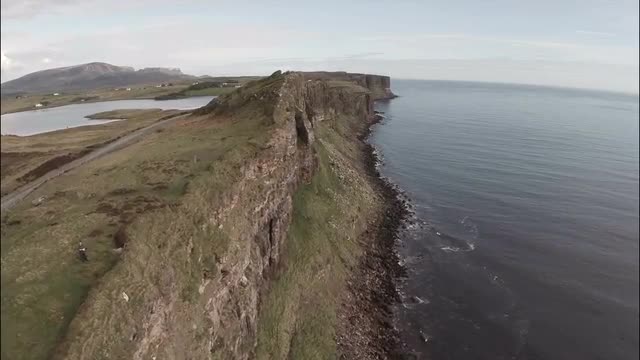Cinematic aerial shot looking over the edge of a cliff on Skye in Scotland with a dramatic coastline