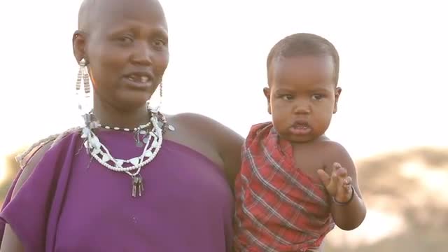 Maasai mother picks up child in traditional clothing