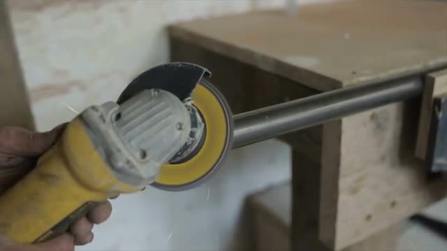 Man in workshop using an angle grinder on a length of steel tube in a vice