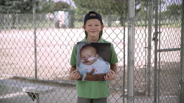 Slow motion push of boy holding up picture of himself as baby and smiling.