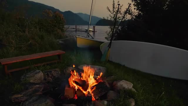 Burning campfire, bench and surfboard near lake