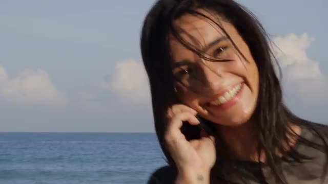 Hispanic woman talking on cell phone near ocean