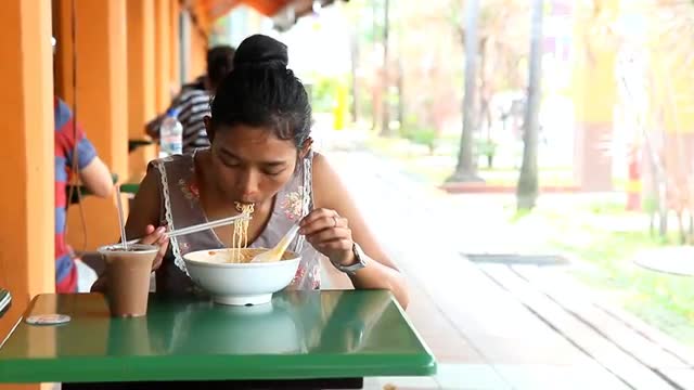 Young Asian woman eating a bowl of noodles