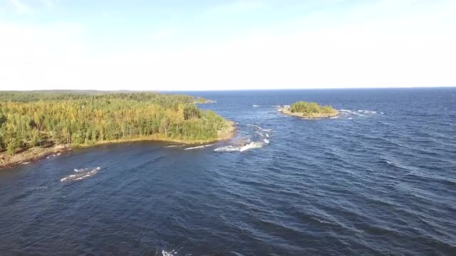 Aerial View of Blue Water and Waves Rolling Onto Rocky Island Shores and Into Bay