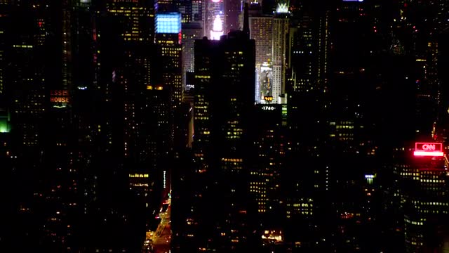 AERIAL side POV past buildings and streets with traffic toward Times square at night