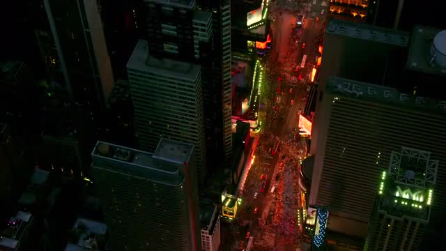 MEDIUM to OVERHEAD POV AERIAL over streets and buildings of Times Square at night