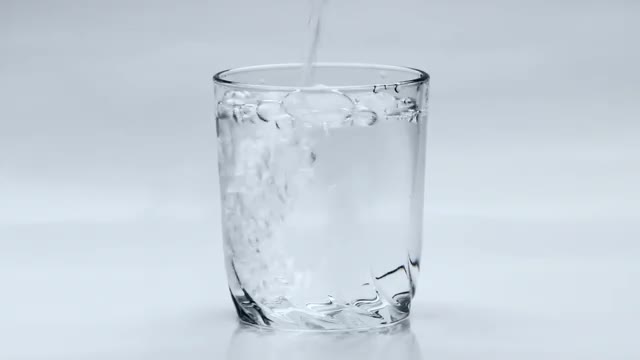 Pouring Water Into Transparent Glass on White Background