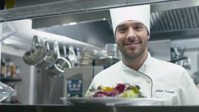 Happy professional chef in a commercial kitchen in a restaurant or hotel is serving salad. 