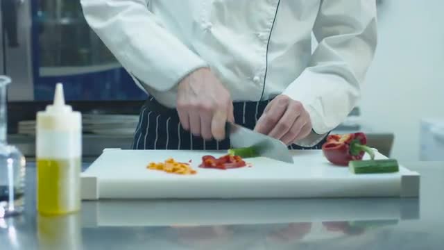 Professional chef in a commercial kitchen in a restaurant or hotel is slicing green vegetables