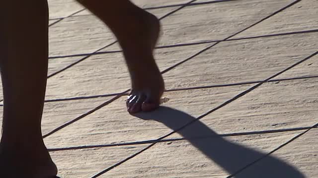 Barefoot woman walks across sun terrace leaving wet footprint behind, slow motion
