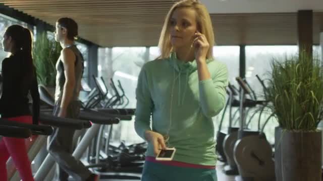 Attractive caucasian girl is starting to run on the treadmill in the sport gym with earphones. 