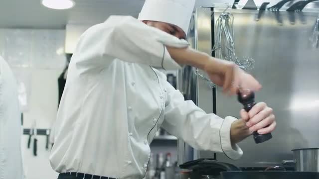 Professional chef in a commercial kitchen in a restaurant or hotel is preparing food on a pan