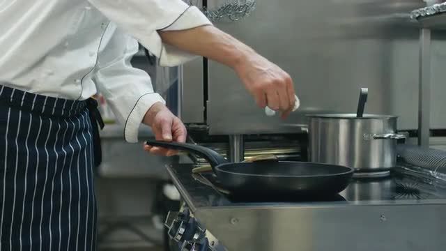 Professional chef in a commercial kitchen in a restaurant or hotel is preparing food on a pan. 