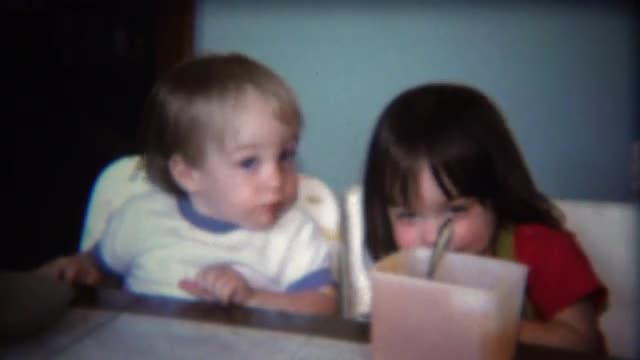 1971: Baby siblings sharing food from square plastic tupperware bowl.