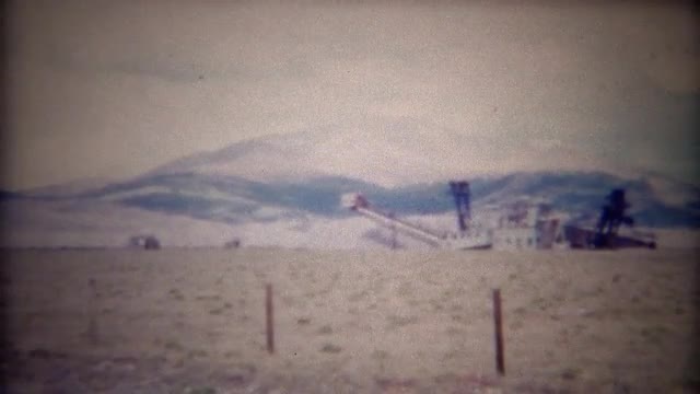 1956: Bucket line gold mining dredge in mountainous region. 