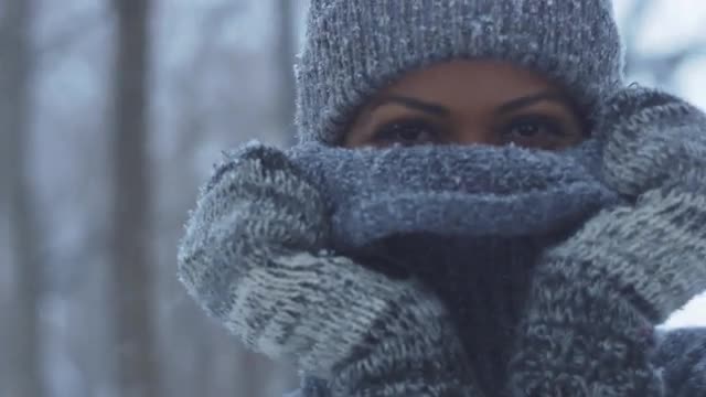 Beautiful girl smiling behind sweater at camera in snowstorm