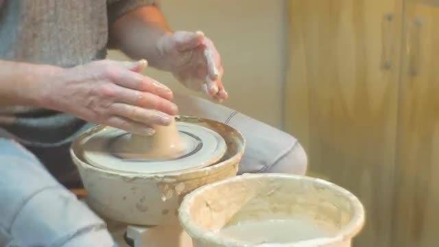 Male Feet in a Sneakers are Rotating a Wheel Man is Molding a Clay Pot Working on a Pottery Wheel Te