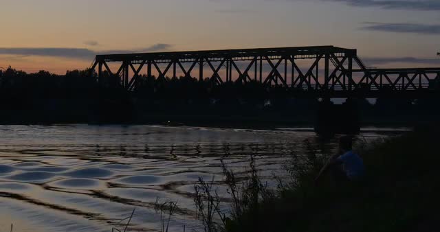 Man in White is Sitting on the River Bank Water Bike Turns River Pond Rippling Water Trees' Silh