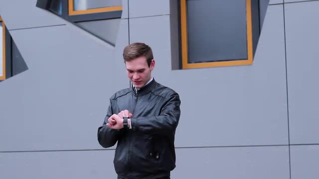 Very Nice Man Using Smart Watches. he Presses a Finger on the Screen, Standing Near the Office Build