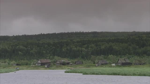 Medium shot of farm buildings on edge of lake on a cloudy day