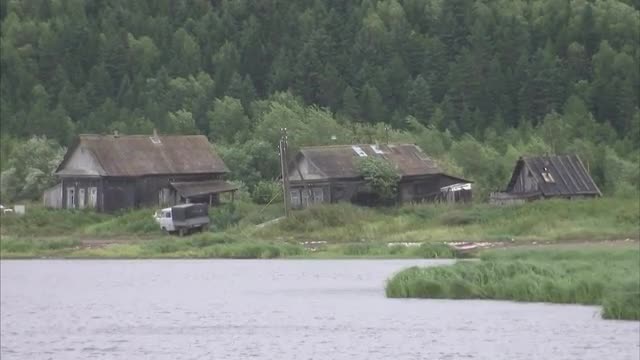Medium/Long shot of birds flying in front of farm buildings on edge of lake